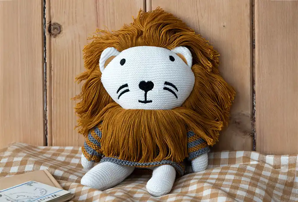 A beautifully knitted lion, crafted from soft cotton, features a delicately embroidered face, a fluffy mane, and a charming grey-and-brown striped top.