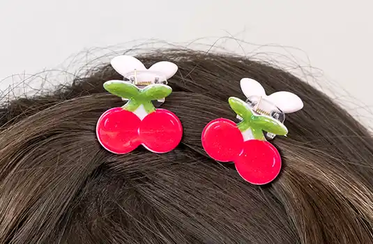 Red cherry-shaped hair clips with green stems and small pink clasps.