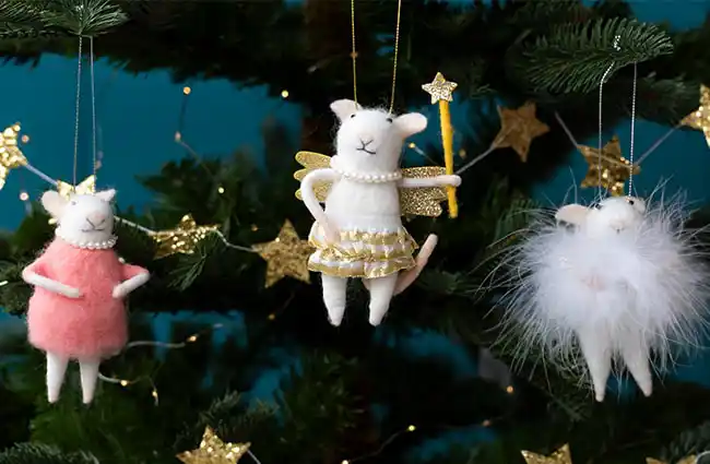 Mice decorations hanging on a green Christmas tree decorated with small gold star ornaments and fairy lights.