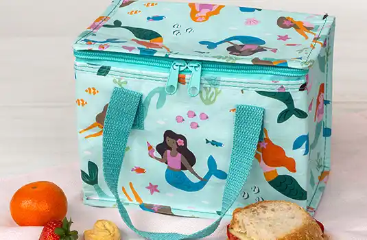 Blue insulated lunch bag with mermaid design, next to fruit and a sandwich.