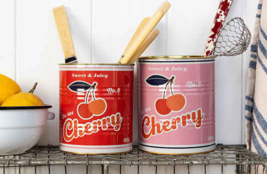 Two retro-style storage cans labeled "Cherry" with cherry illustrations, one red and one pink, placed on a wire shelf.