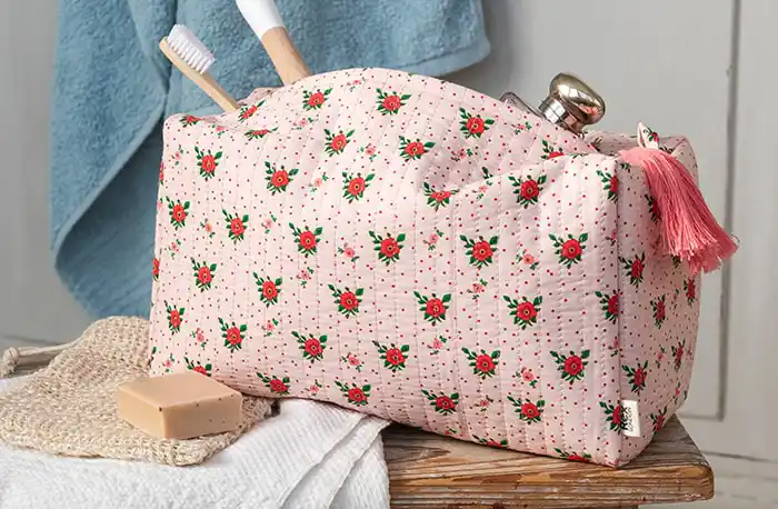 A quilted fabric toiletry bag with pink background and red floral pattern.