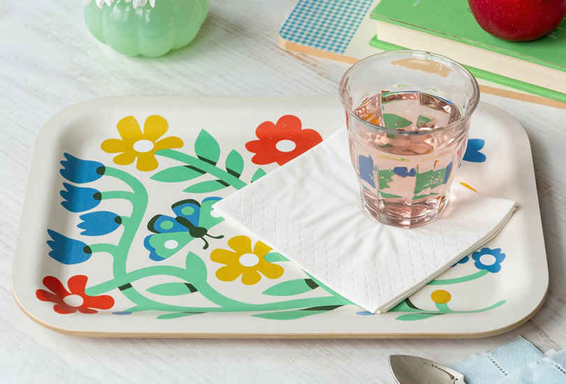 Wooden serving tray holding a glass of water and a folded white napkin on a colourful floral-patterned surface.