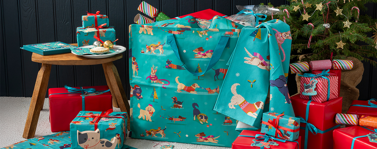 Christmas-themed gift scene with dog-patterned teal bags, wrapped presents, and festive decorations.