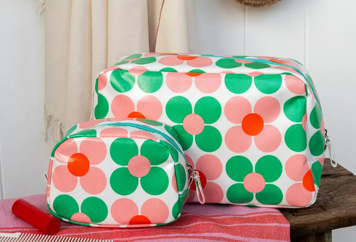 Two pink‑and‑green daisy-print makeup and wash bags made from easy‑to‑wipe‑clean oilcloth. 