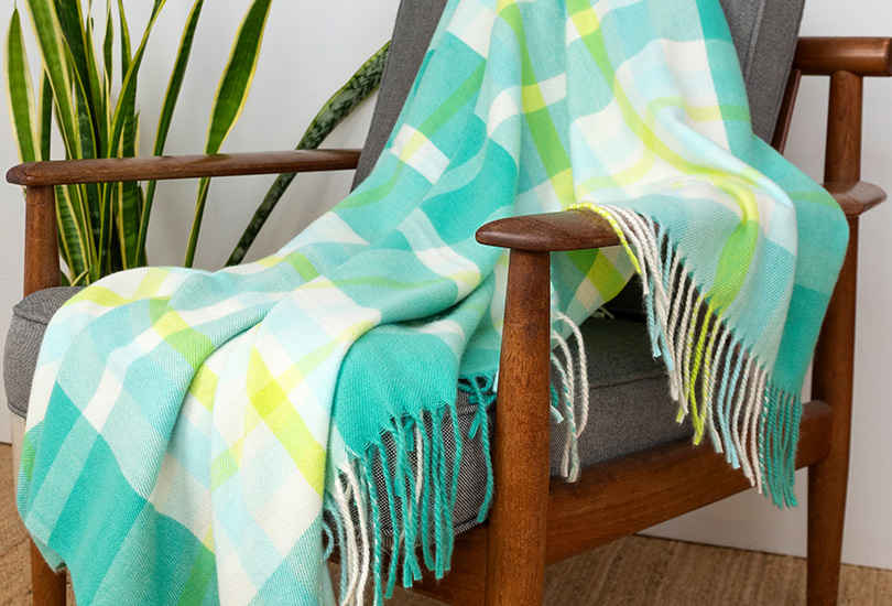 Green plaid throw blanket with fringe draped over a wooden armchair.
