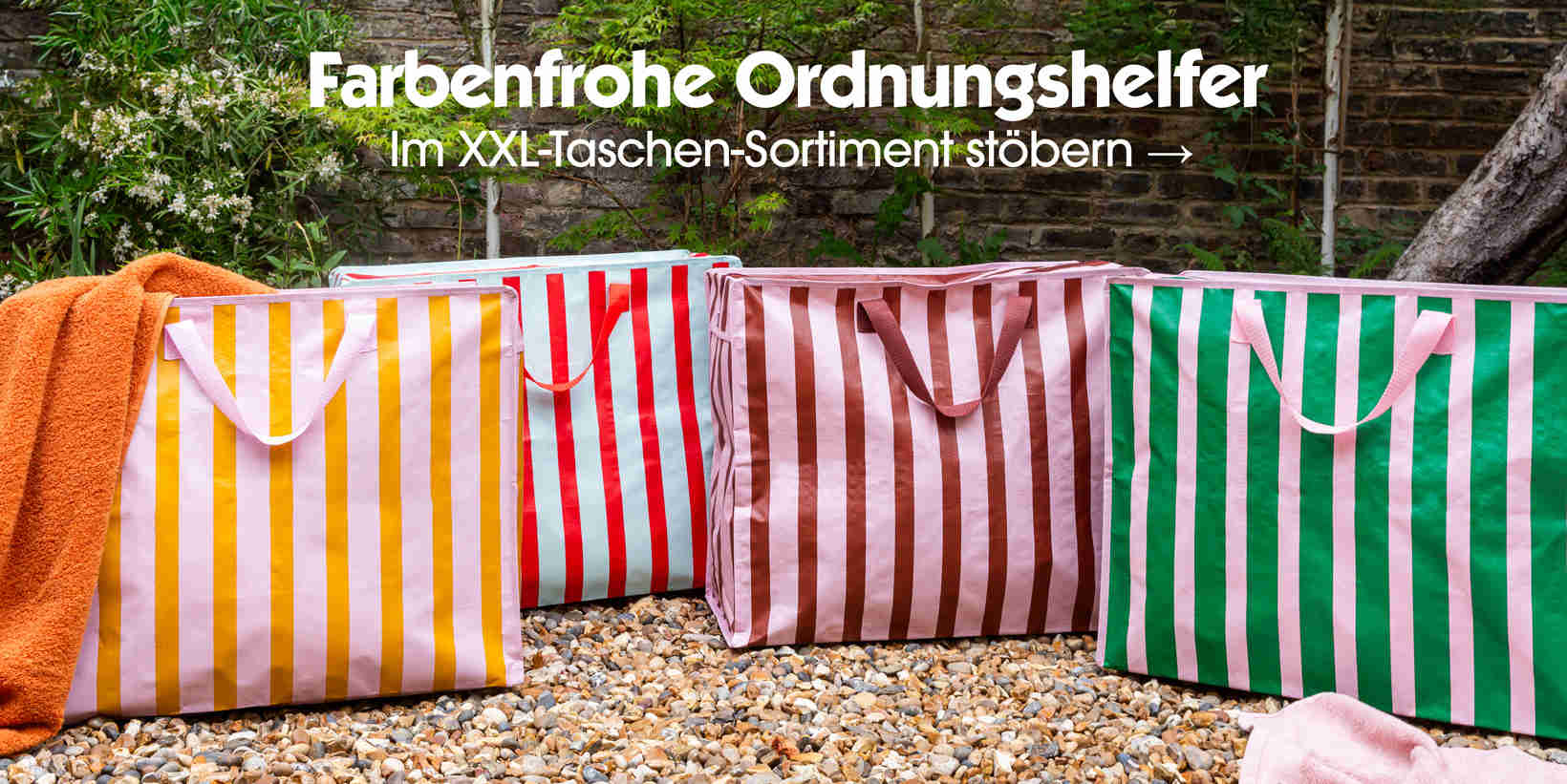 Large colourful striped jumbo storage bags displayed outdoors on gravel with greenery background, promoting storage solutions collection