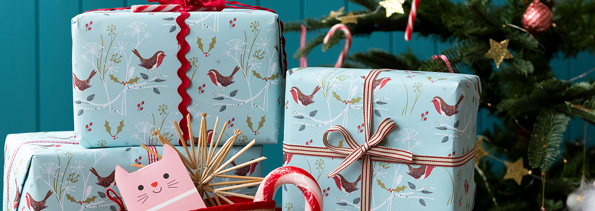 Stack of Christmas presents wrapped in light blue paper with bird and holly patterns, tied with red and white ribbons