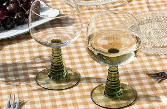 Two stemmed wine glasses filled with white wine, placed on a patterned tablecloth outdoors.