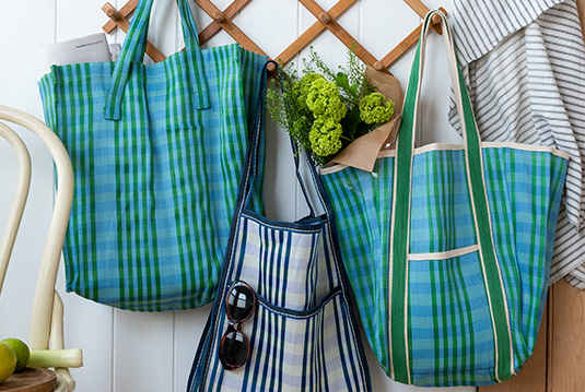 Assorted green and blue checked travel bags and shopping bag hanging on hooks.