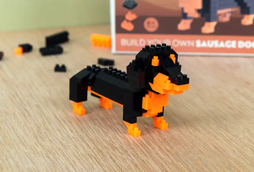 a buildable sausage dog model made from black and orange plastic bricks