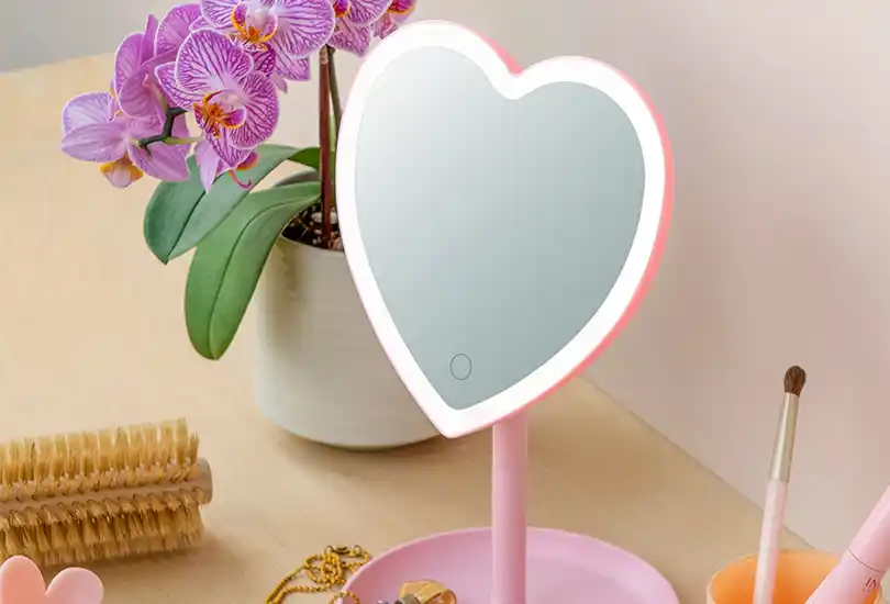 Pink heart-shaped light-up vanity mirror on a wooden surface.