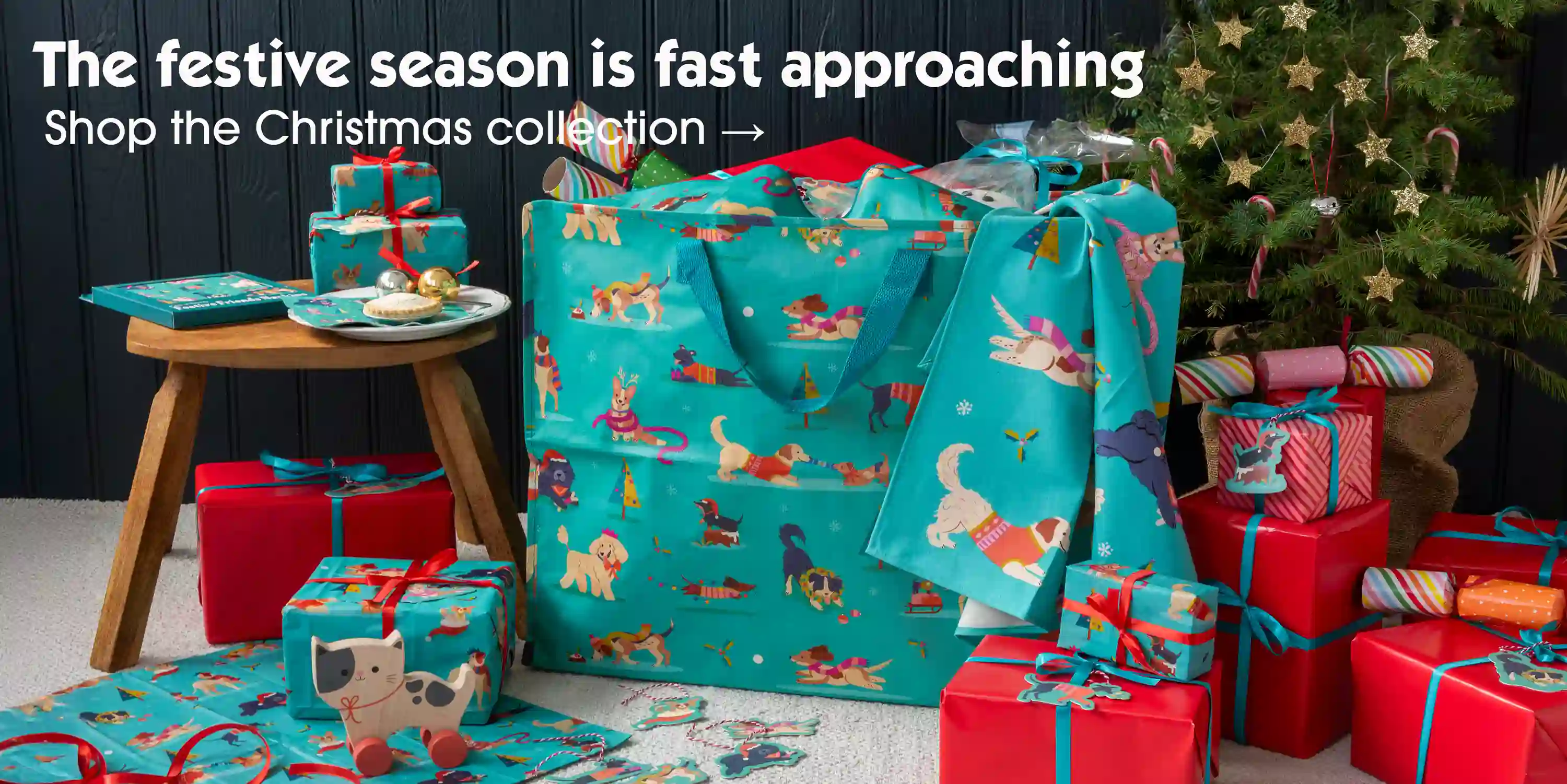 Festive-themed gift scene with dog-patterned teal bags, wrapped presents, and festive decorations.