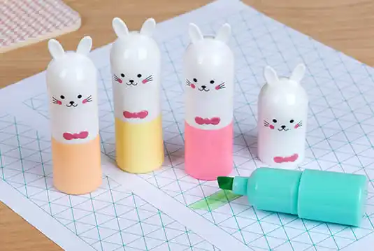 Four cute bunny‑shaped highlighters with pastel bottoms placed on patterned paper, with one green highlighter uncapped beside them.