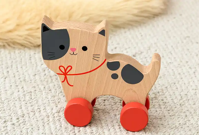 Wooden toy cat on red wheels placed on a carpet.