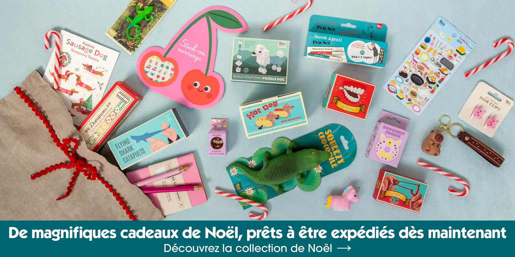 Flat lay of assorted stocking filler gifts on a light blue background, including candy canes, novelty toys, stickers, mini games, and beauty items.