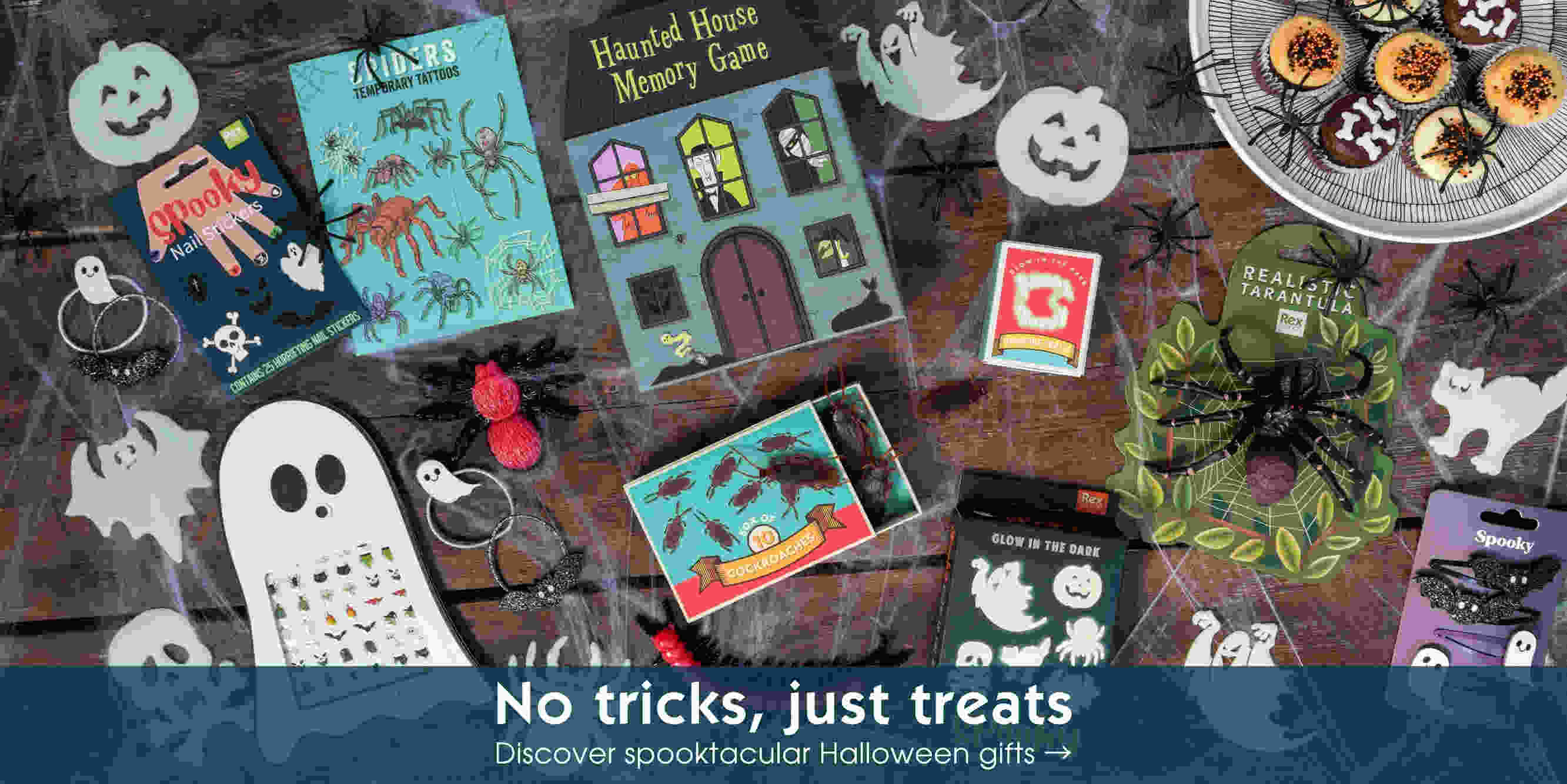 Halloween-themed flat lay featuring spider and creepy crawly toys, boxes of temporary tattoos, plastic insects, and a spider web-decorated dessert tray with Twinkie-style treats.