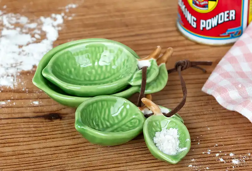 Lime‑coloured leaf‑shaped ceramic measuring spoons stacked on a wooden surface.