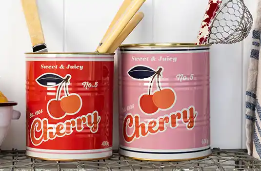 Two retro-style storage cans labeled "Cherry" with cherry illustrations, one red and one pink, placed on a wire shelf