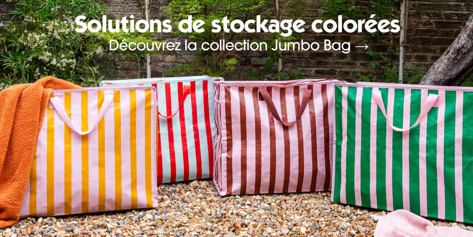 Large colourful striped jumbo storage bags displayed outdoors on gravel with greenery background, promoting storage solutions collection